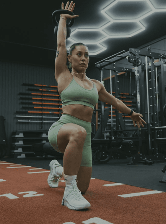Elena Rossi holding a kettlebell overhead in a kneeling lunge