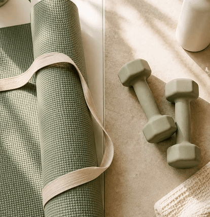 Sage yoga mat with linen strap beside matte dumbbells